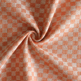Close up of draped woven fabric with small scale checkerboard pattern in white and bright orange. 
