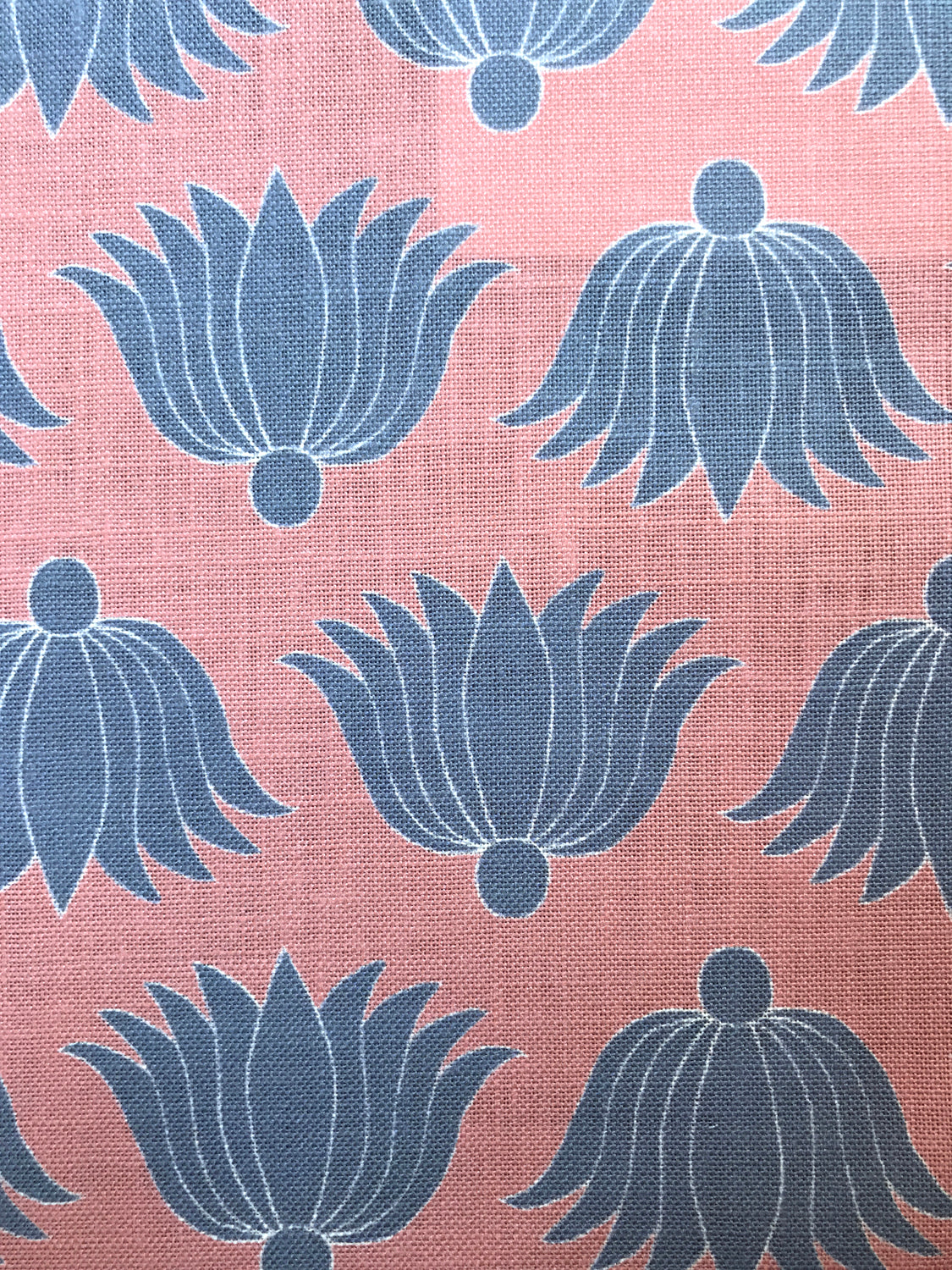 Detail of fabric in a repeating lotus print in blue and white on a coral field.