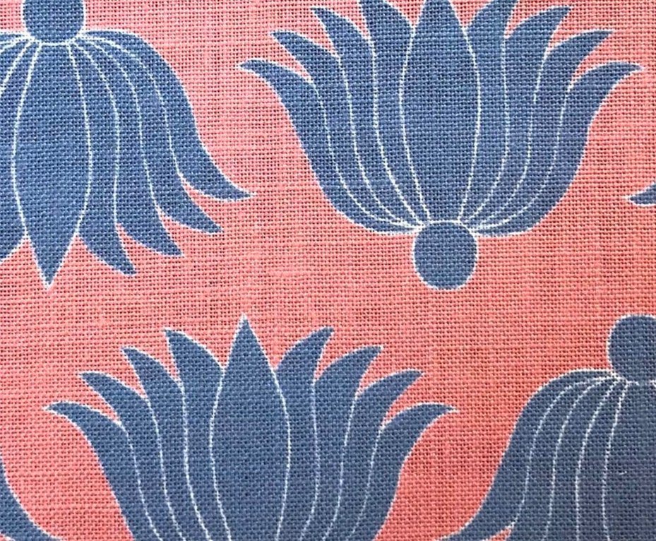 Detail of fabric in a repeating lotus print in blue and white on a coral field.