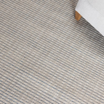 Close-up of a textured striped gray carpet with a white chair corner. 
