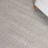 Close-up of a textured striped gray carpet with a white chair corner. 