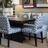 Dining room with patterned chairs around a wooden table, lamp, and framed pictures on the wall.