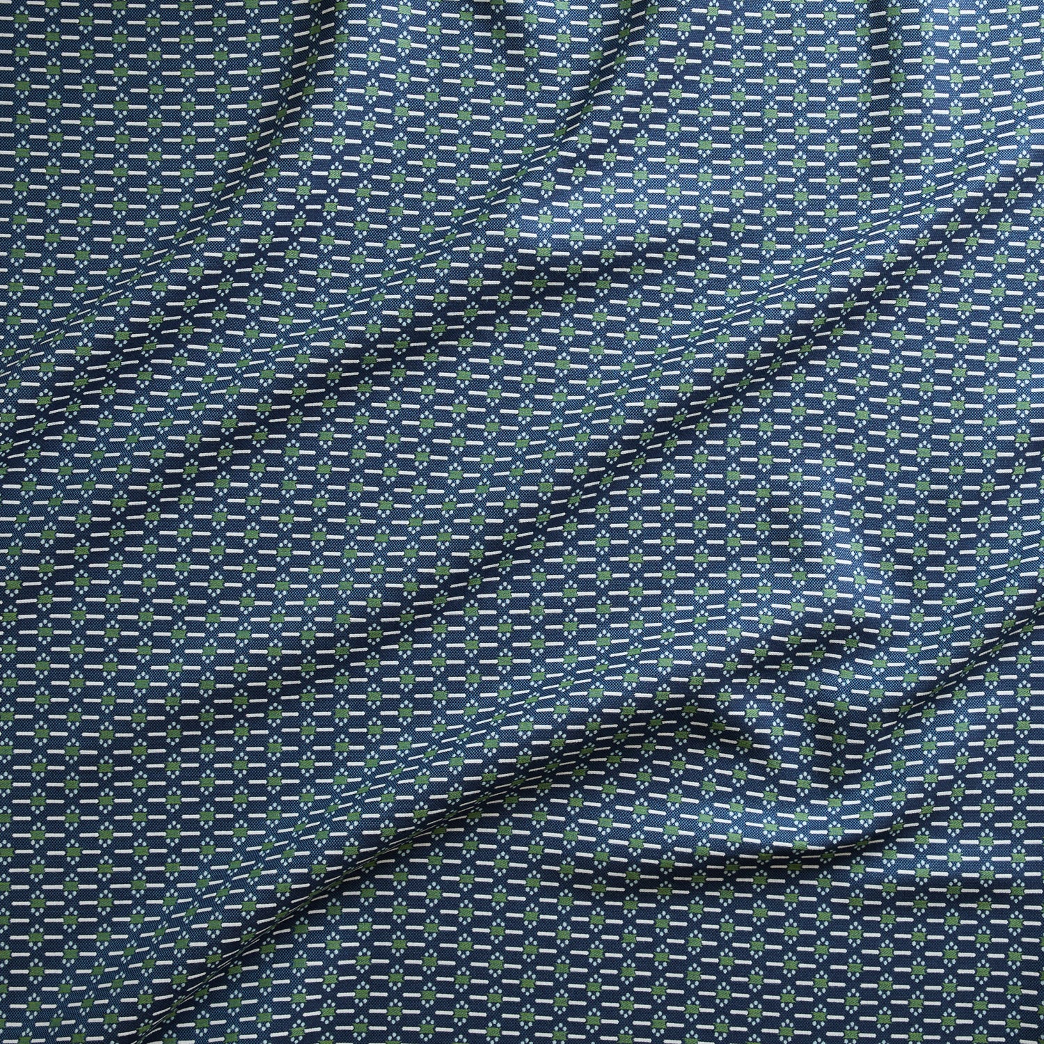 Close up of gently draped woven Indoor-Outdoor fabric with small scale geometric ditsy print in green and ivory on navy blue. 