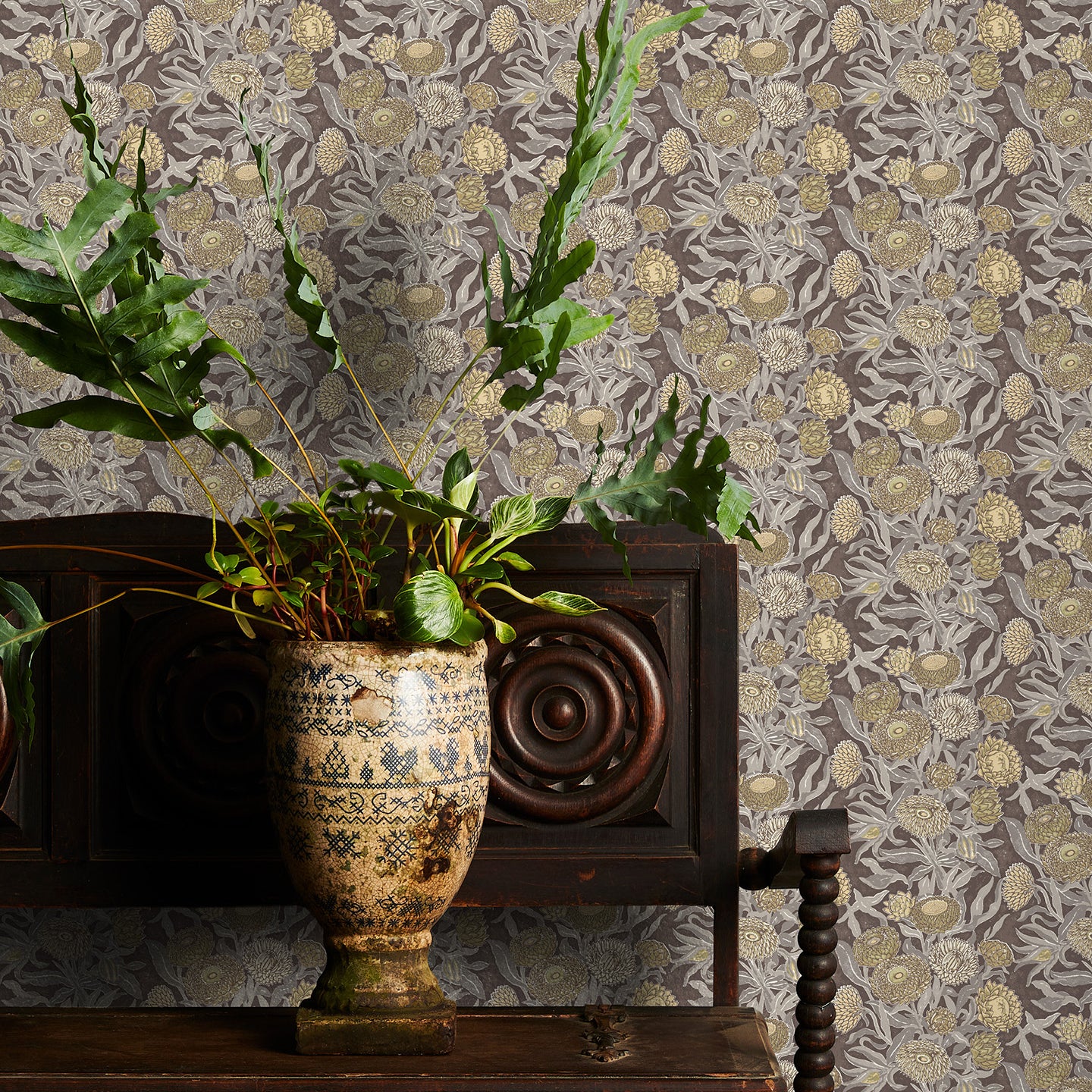 Decorative wallpaper with brown floral pattern, wooden cabinet with plants, and ornate vase.
