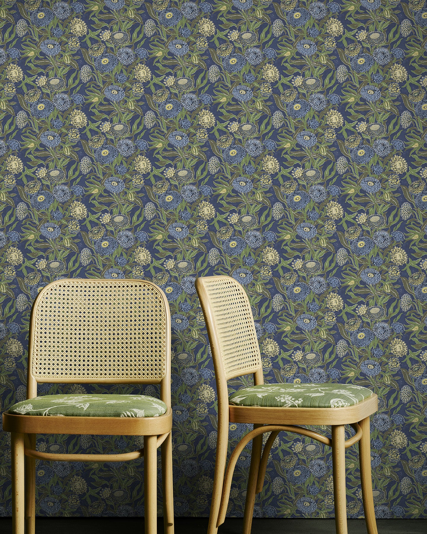 Two wooden chairs with floral cushions against a green and blue floral-patterned wallpaper