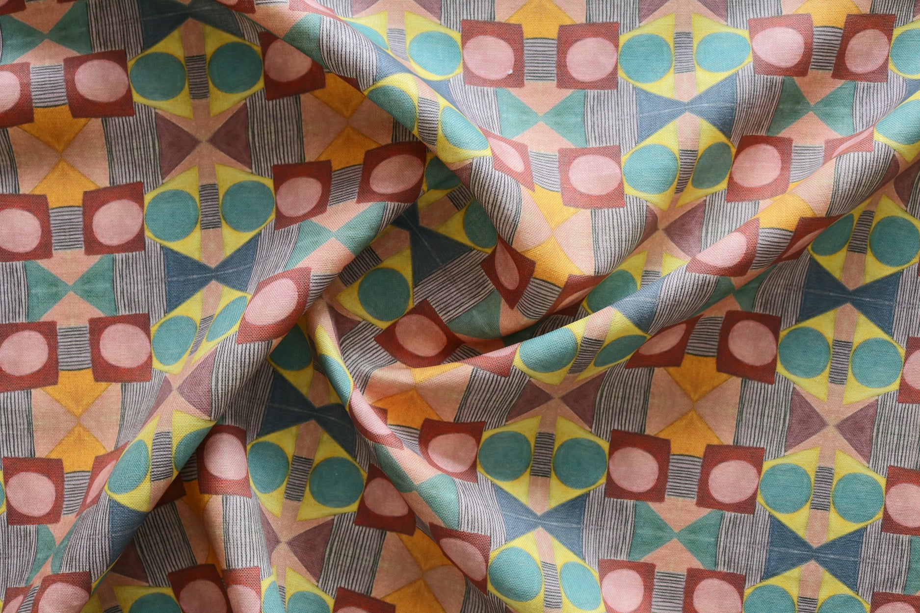 Close up of gently draped printed fabric with a complex geometric pattern with pink, red, blue, yellow, orange and turquoise