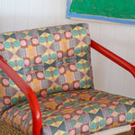 Red metal frame side chair with bold geometric print upholstery against a white paneled wall and bold geometric drawing. 