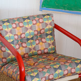 Red metal frame side chair with bold geometric print upholstery against a white paneled wall and bold geometric drawing. 