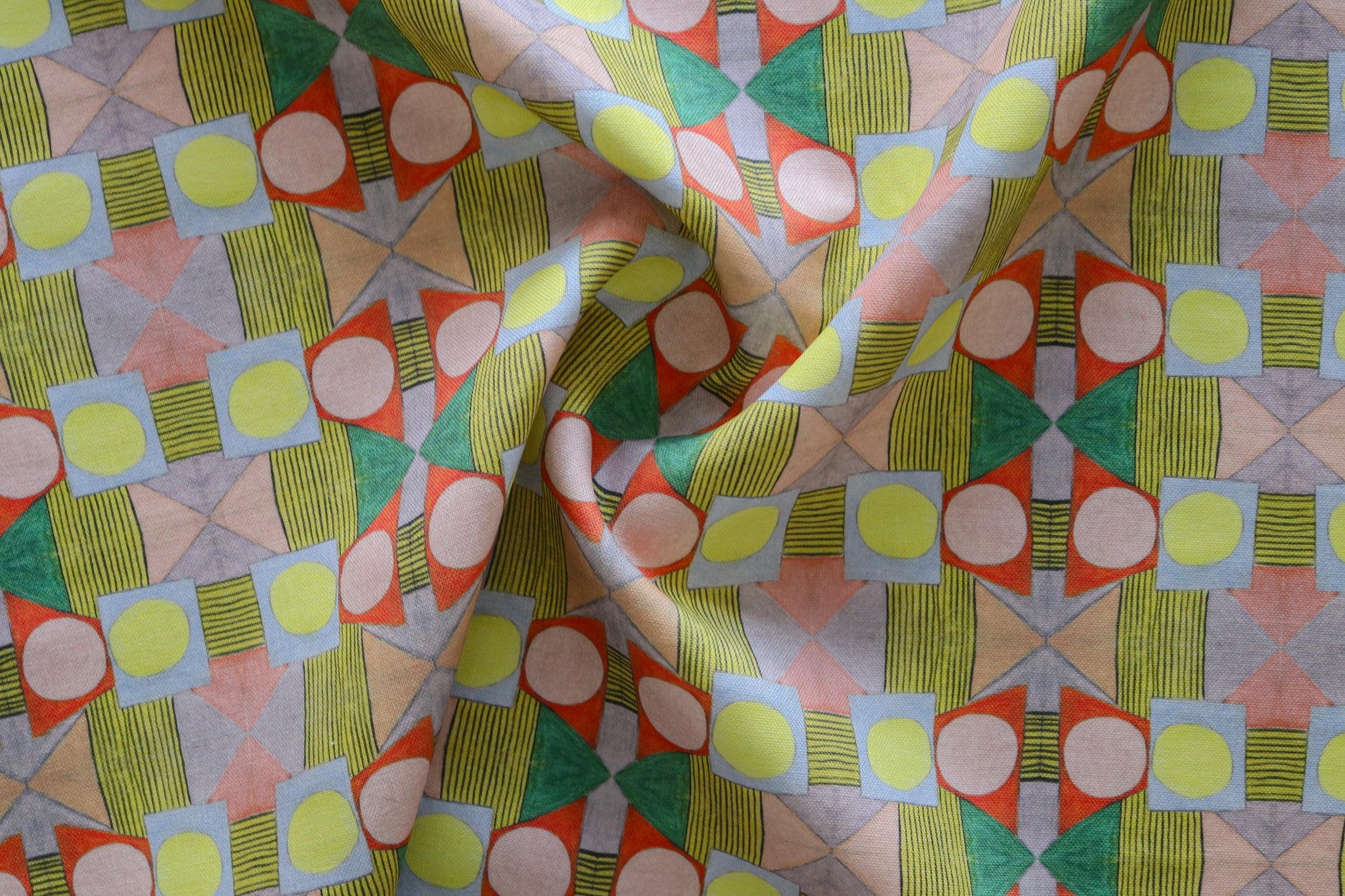 Close up of gently draped printed fabric with a complex geometric pattern with pink, red, light purple, green and yellow. 