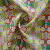 Close up of gently draped printed fabric with a complex geometric pattern with pink, red, light purple, green and yellow. 