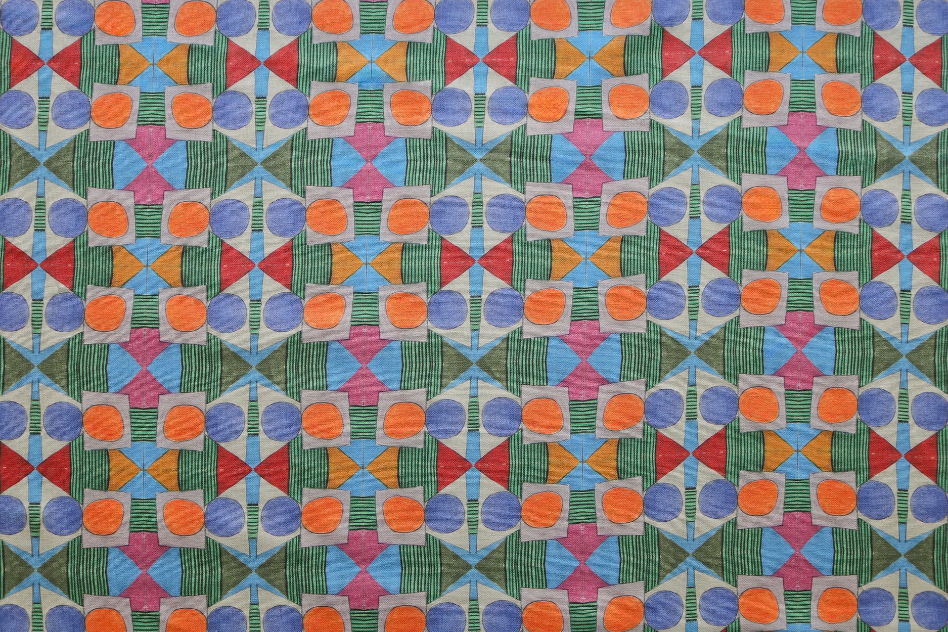 Close up of printed fabric with a complex geometric pattern with blue, orange, green, pink and red. 