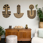 Living room scene with three black and tan sculptural woven panels, ornately carved wooden chest, baskets with house plans, white upholstered side chair and a stripe patterned footstool in beige. 