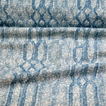 Draped fabric coming off a roll with monochomatic geometric stripe and mottled textural background in shades of  blue.
