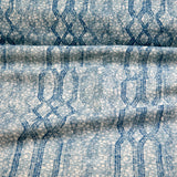 Draped fabric coming off a roll with monochomatic geometric stripe and mottled textural background in shades of  blue.