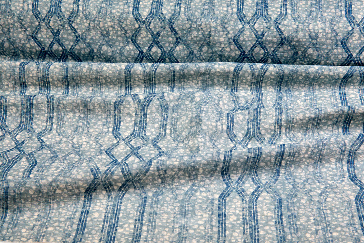 Draped fabric coming off a roll with monochomatic geometric stripe and mottled textural background in shades of  blue.
