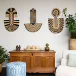 Living room scene with three black and tan sculptural woven panels, ornately carved wooden chest, baskets with house plans, white upholstered side chair and a stripe patterned footstool in blue.