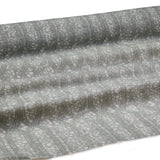 Draped fabric coming off a roll with monochomatic geometric stripe and mottled textural background in shades of grey.