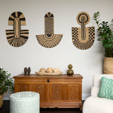 Living room scene with three black and tan sculptural woven panels, ornately carved wooden chest, baskets with house plans, white upholstered side chair and a stripe patterned footstool in pale grey.