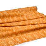 Draped fabric coming off a roll with monochomatic geometric stripe and mottled textural background in shades of  orange.
