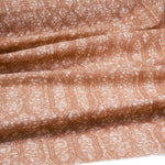 Draped fabric coming off a roll with monochomatic geometric stripe and mottled textural background in shades of  orange.