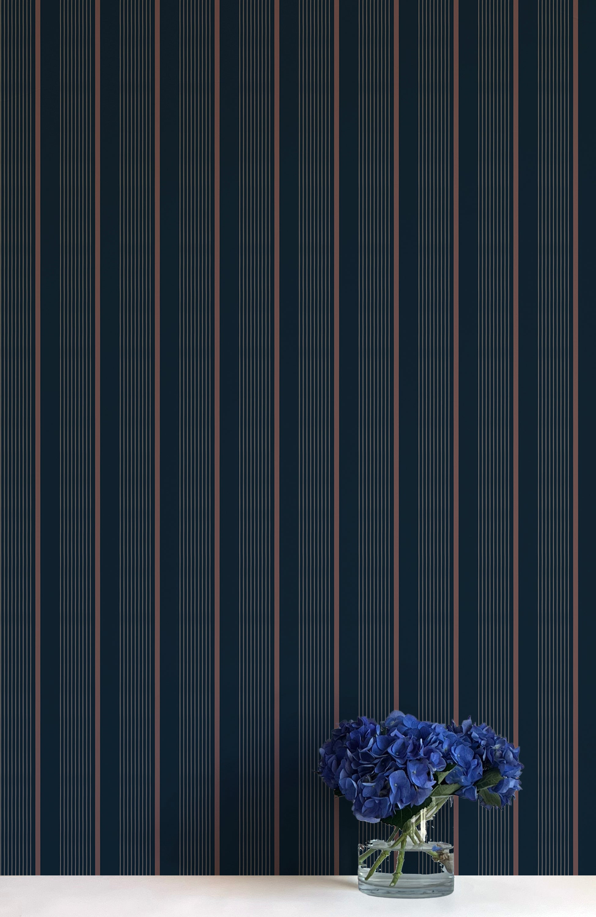Navy blue wallpaper with thin white stripes and a vase of blue flowers on a white surface.