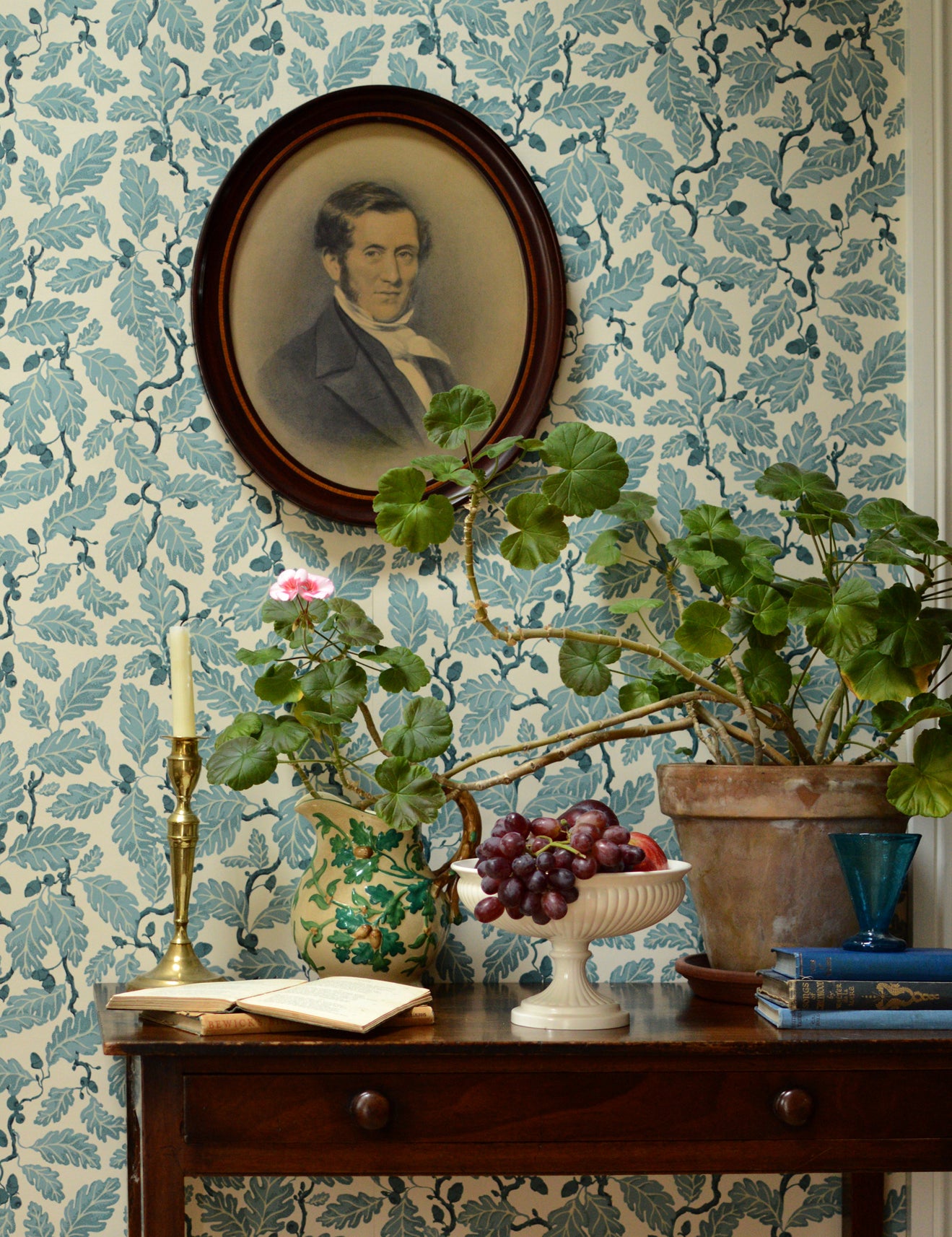 Decorative room interior with floral wallpaper, a portrait, and plants on a wooden table.