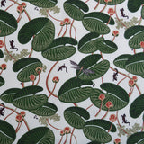 Patterned fabric with green lily pads, red flowers and small creatures on a white background