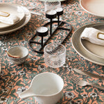 A dining room table covered in a dense floral print in white, tan and green on a light pink field.