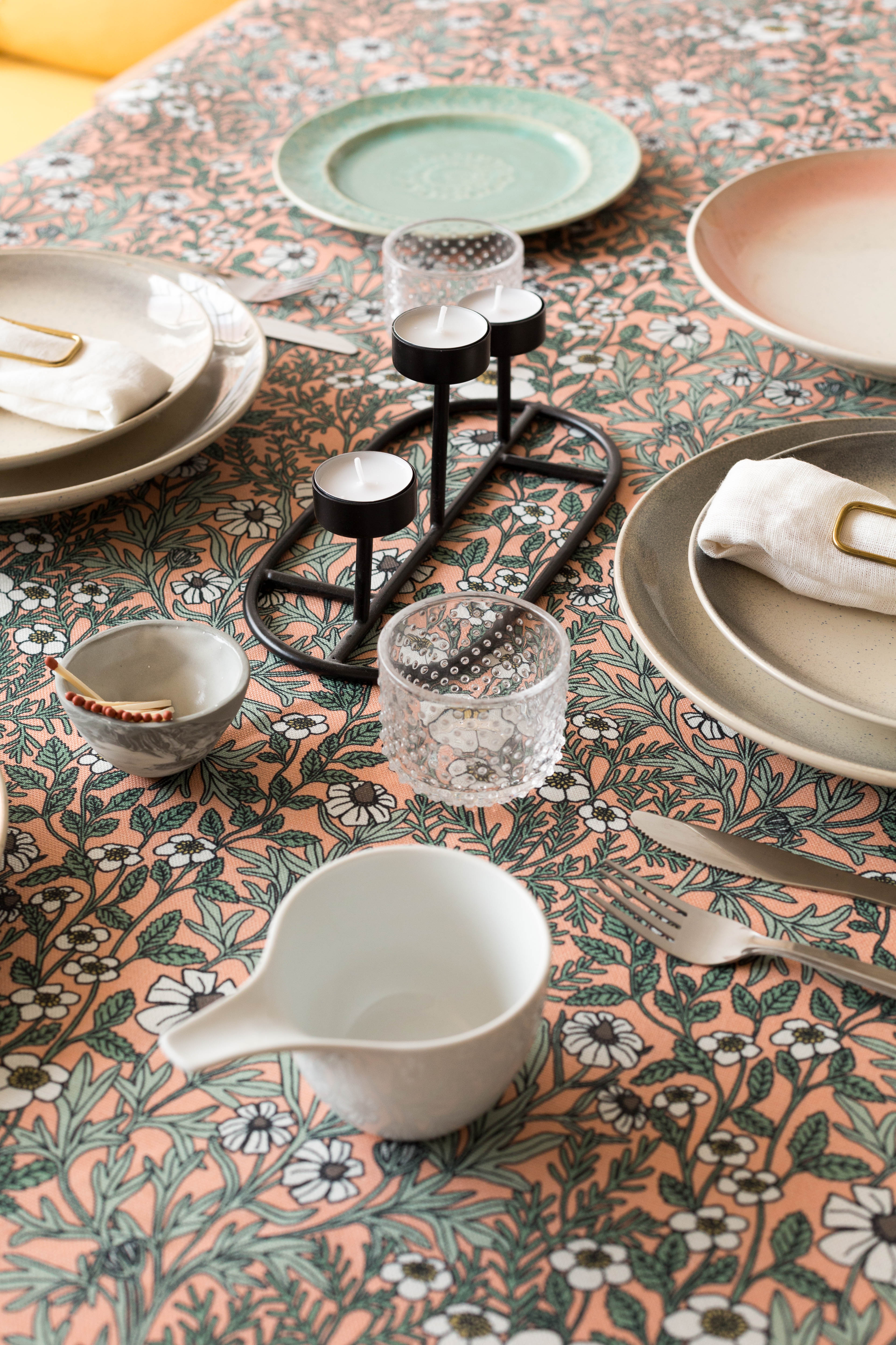 A dining room table covered in a dense floral print in white, tan and green on a light pink field.