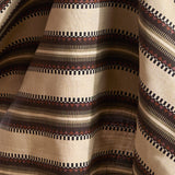 Fabric in complex geometric stripe in brown, tan, orange, light purple and black on a cream field.