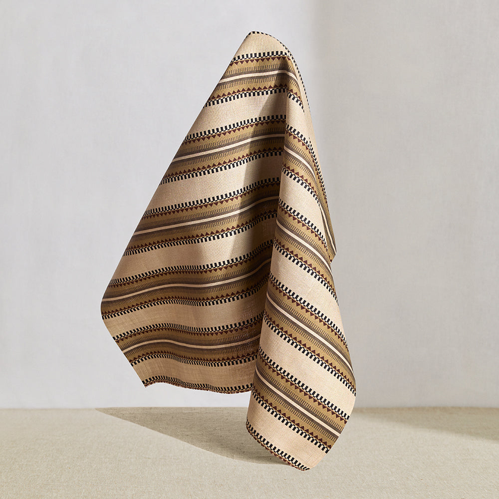 Hanging fabric in a complex geometric stripe in brown, tan, orange, light purple and black on a cream field.