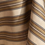 Fabric in a complex geometric stripe in brown, tan, orange, light purple and black on a cream field.