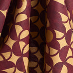 Fabric in a curvilinear art deco inspired pattern in rust red, ochre and ecru.