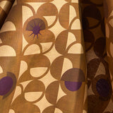 Fabric in a curvilinear art deco inspired pattern in ochre, beige and purple.