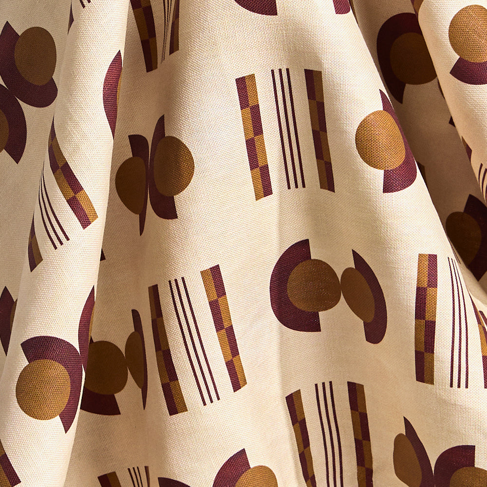 Fabric in a graphic geometric pattern of circles and stripes in maroon and ochre on a cream field. 