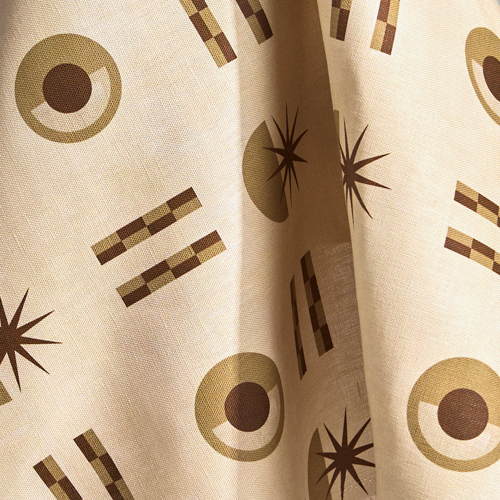 Fabric in a graphic geometric pattern of circles, stars and stripes in taupe and brown on a cream field.