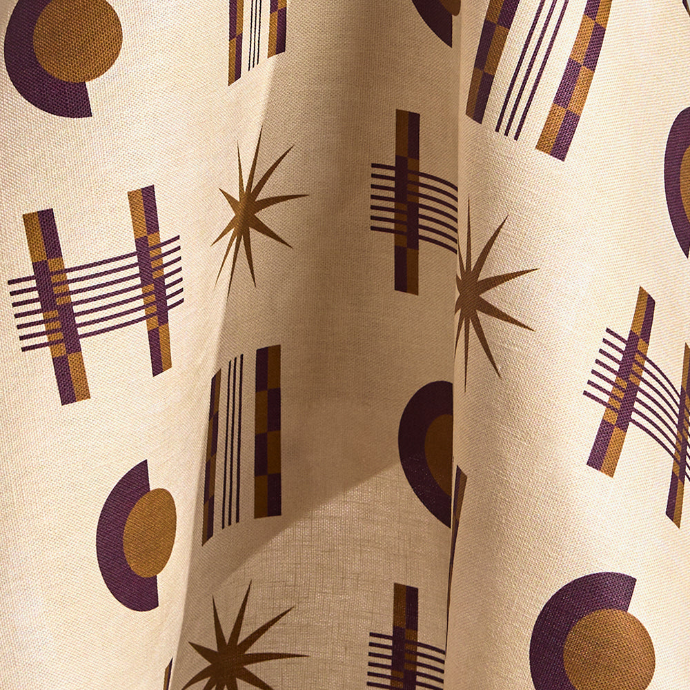 Fabric in a graphic geometric pattern of circles, stars and stripes in purple and ochre on a cream field.