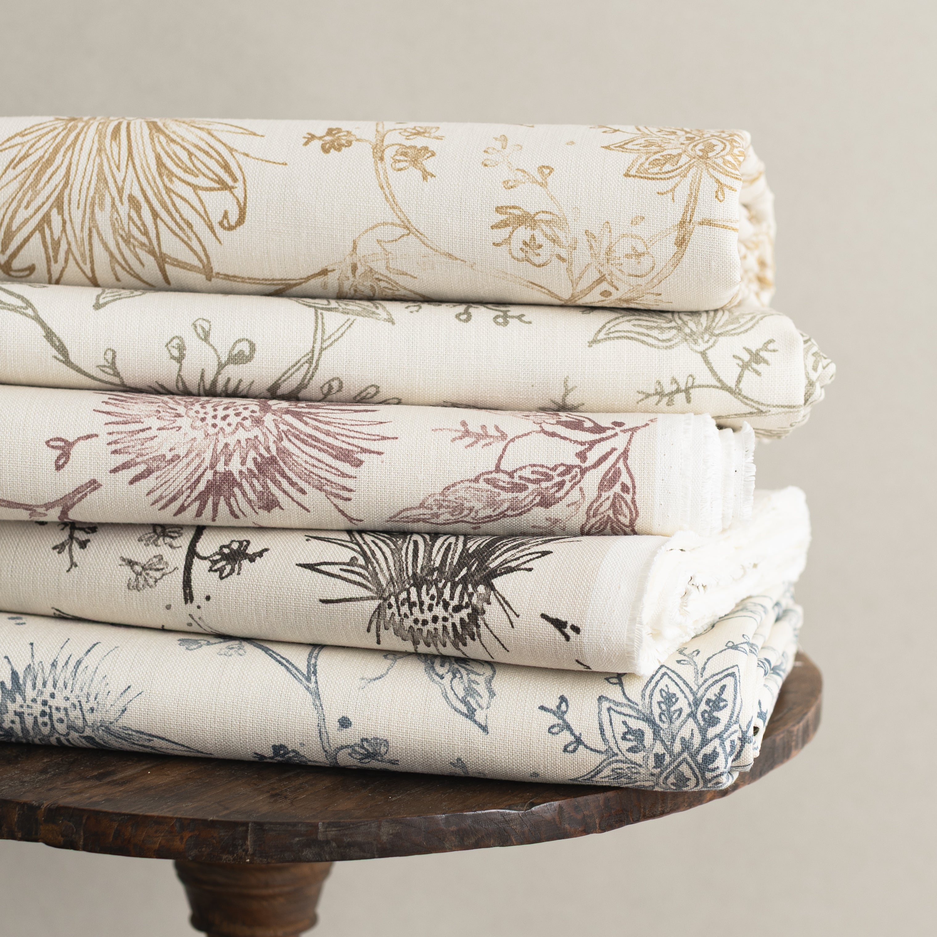 Wooden side table with stacks of folded fabric in floral design in various colors. 