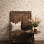 Vintage wooden bench with a plaid pillow and a vase of flowers against a floral wallpapered wall.