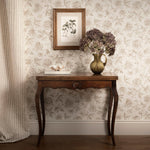 Wooden side table with decorative items against a floral wallpapered wall.