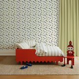 Red children's bed with striped bedding against a black and white floral patterned wall.