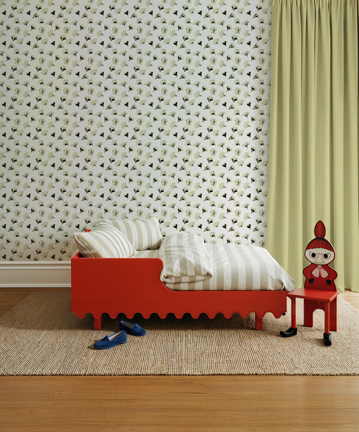 Red children's bed with striped bedding against a black and white floral patterned wall.