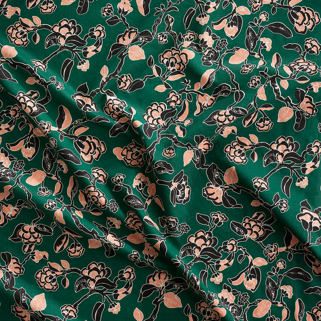 Close up of gently draped printed linen in a hand drawn branch and flower design in black and light pink on emerald green.
