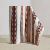 Wallpaper roll in a complex geometric stripe in maroon, ochre, ecru and black on a cream field.