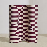 Wallpaper roll in a trompe l'oeil stripe pattern with geometric shapes in cream and burgundy. 