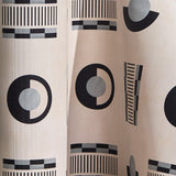 Wallpaper in a graphic geometric pattern of circles, and stripes in black and grey on a cream field.