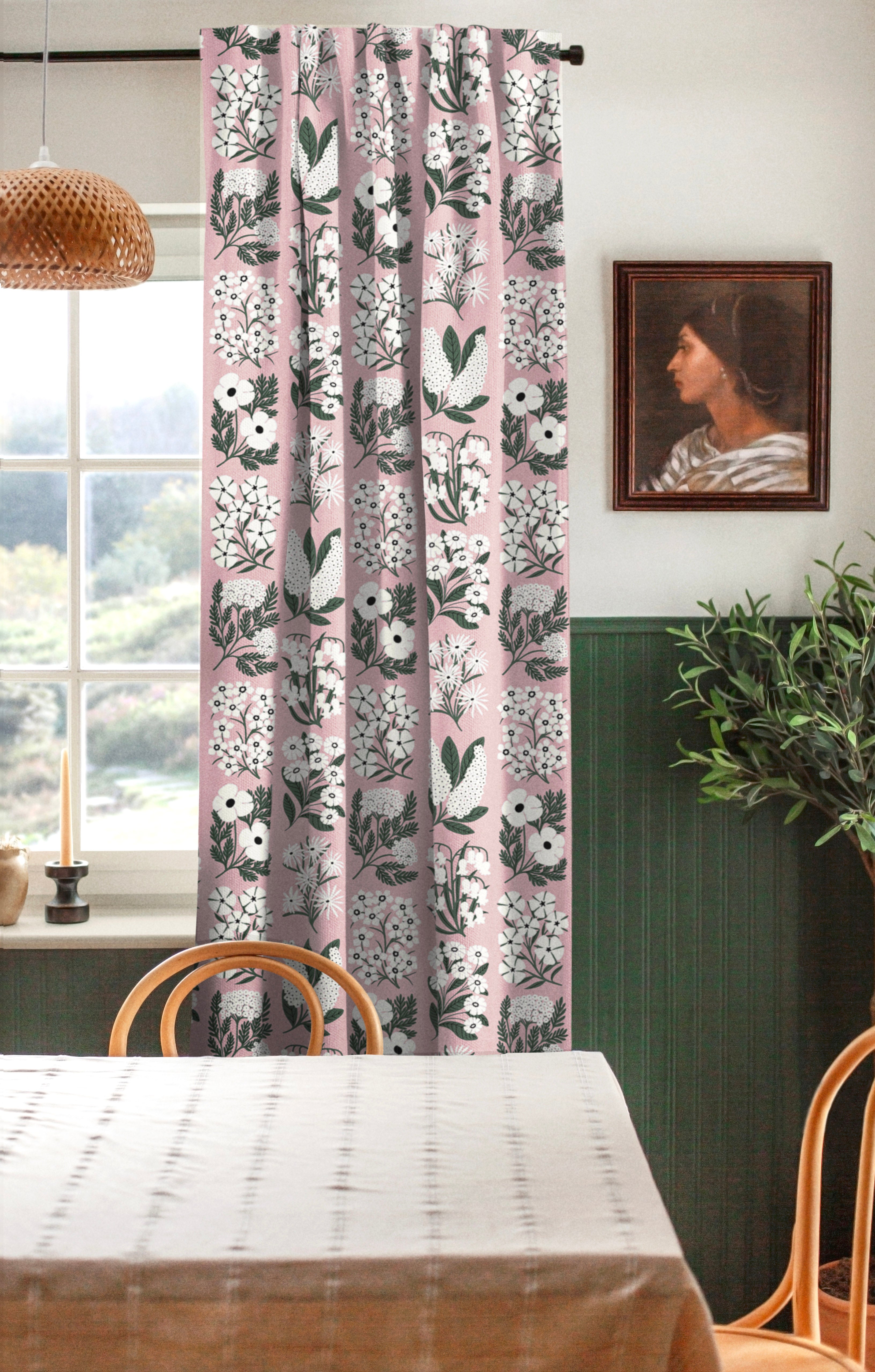 A cozy dining room with a large window and curtains in a minimalist floral grid print in white and green on a pink field.