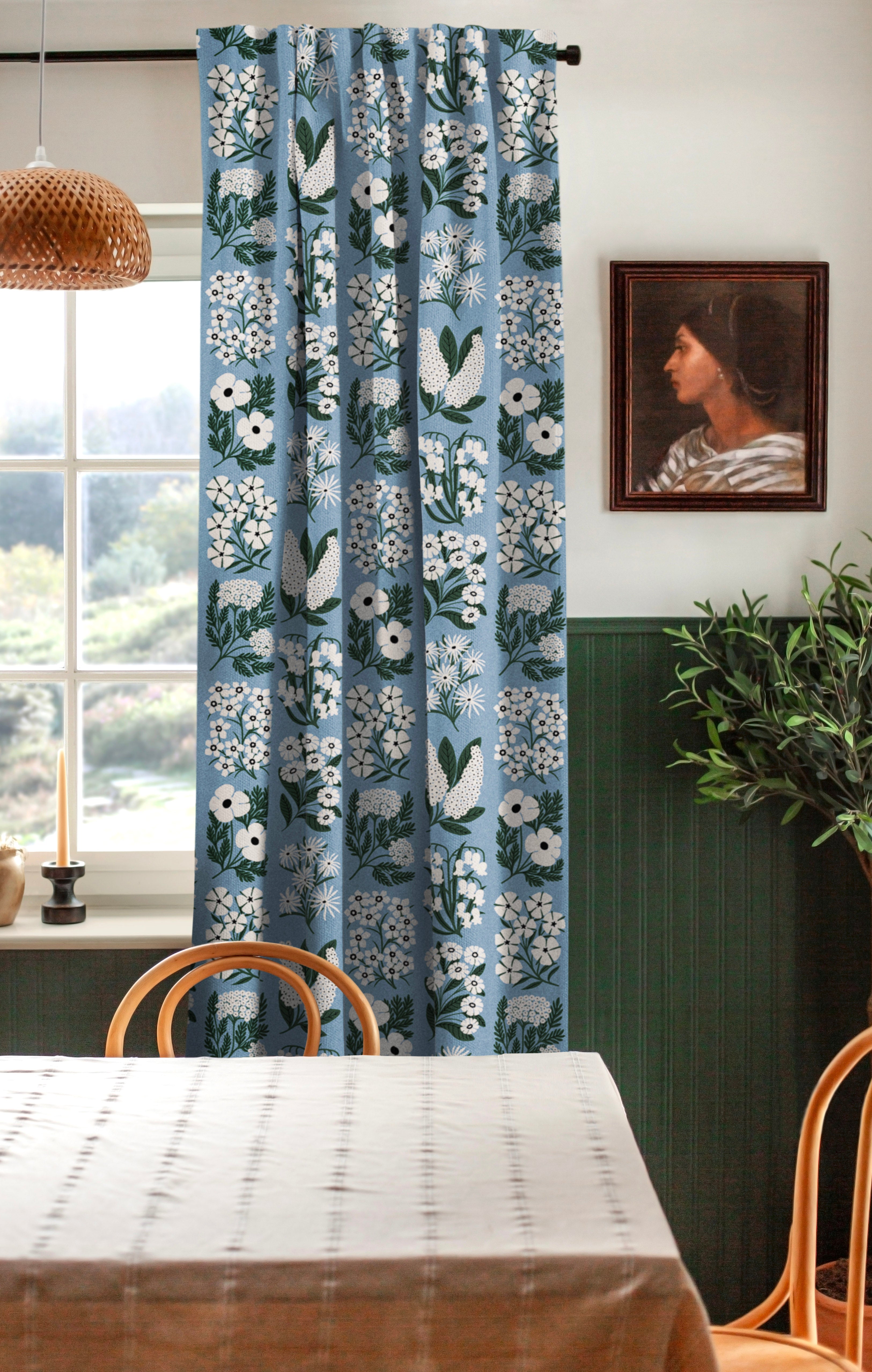 A cozy dining room with a large window and curtains in a minimalist floral grid print in white and green on a blue field.