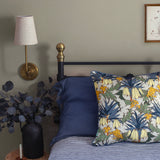 A cozy bedroom tableau with a bed covered in navy and white sheets, with a maximalist floral throw pillow.