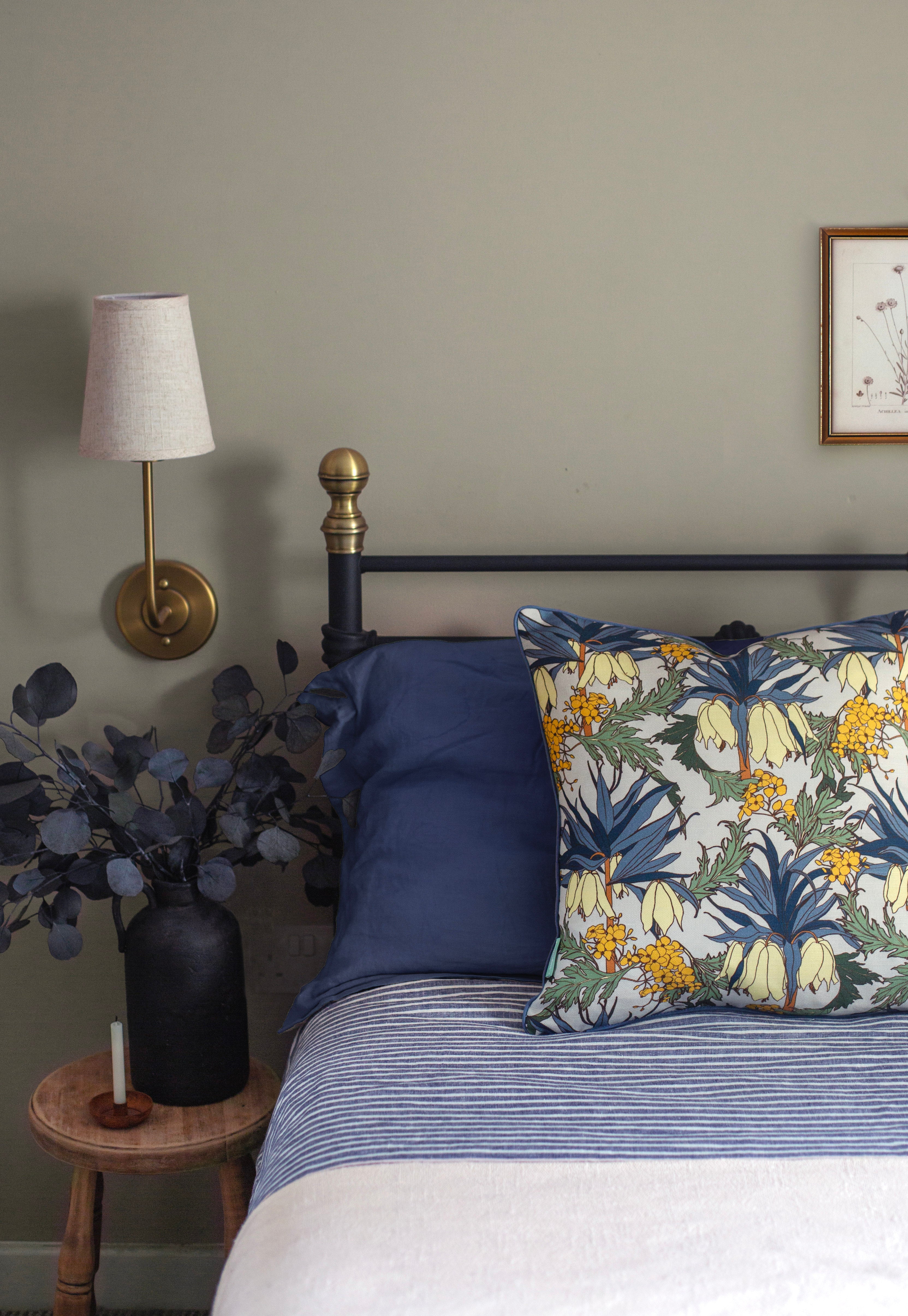 A cozy bedroom tableau with a bed covered in navy and white sheets, with a maximalist floral throw pillow.